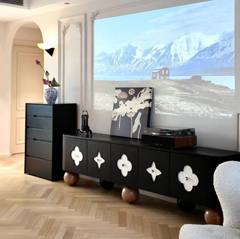 Black media console with floral decorations and wooden legs.