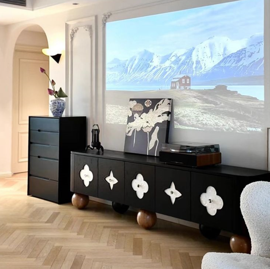 Black media console with floral decorations and wooden legs.